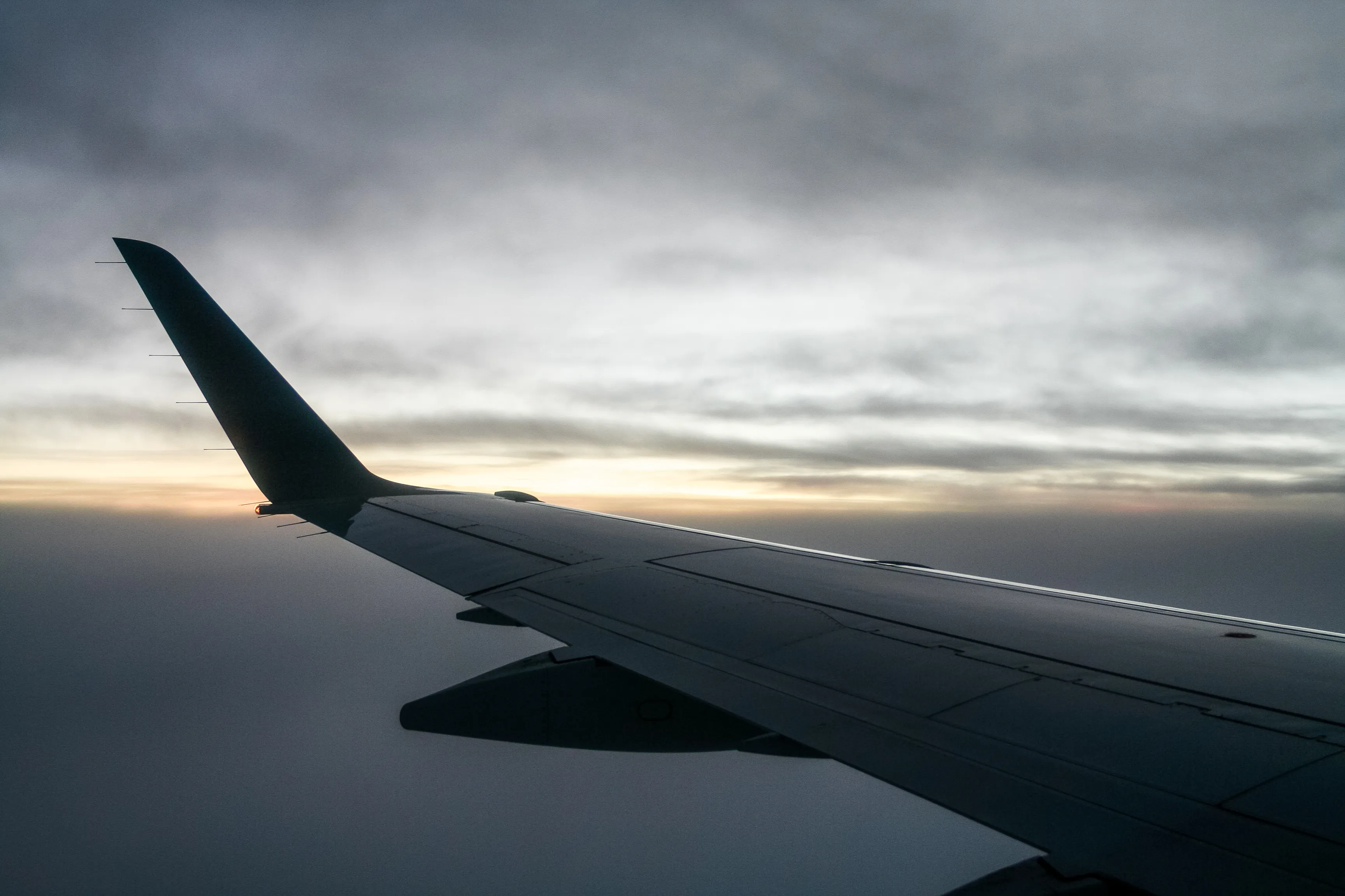 An airplane wing in flight silhouetted against a distant sunrise.